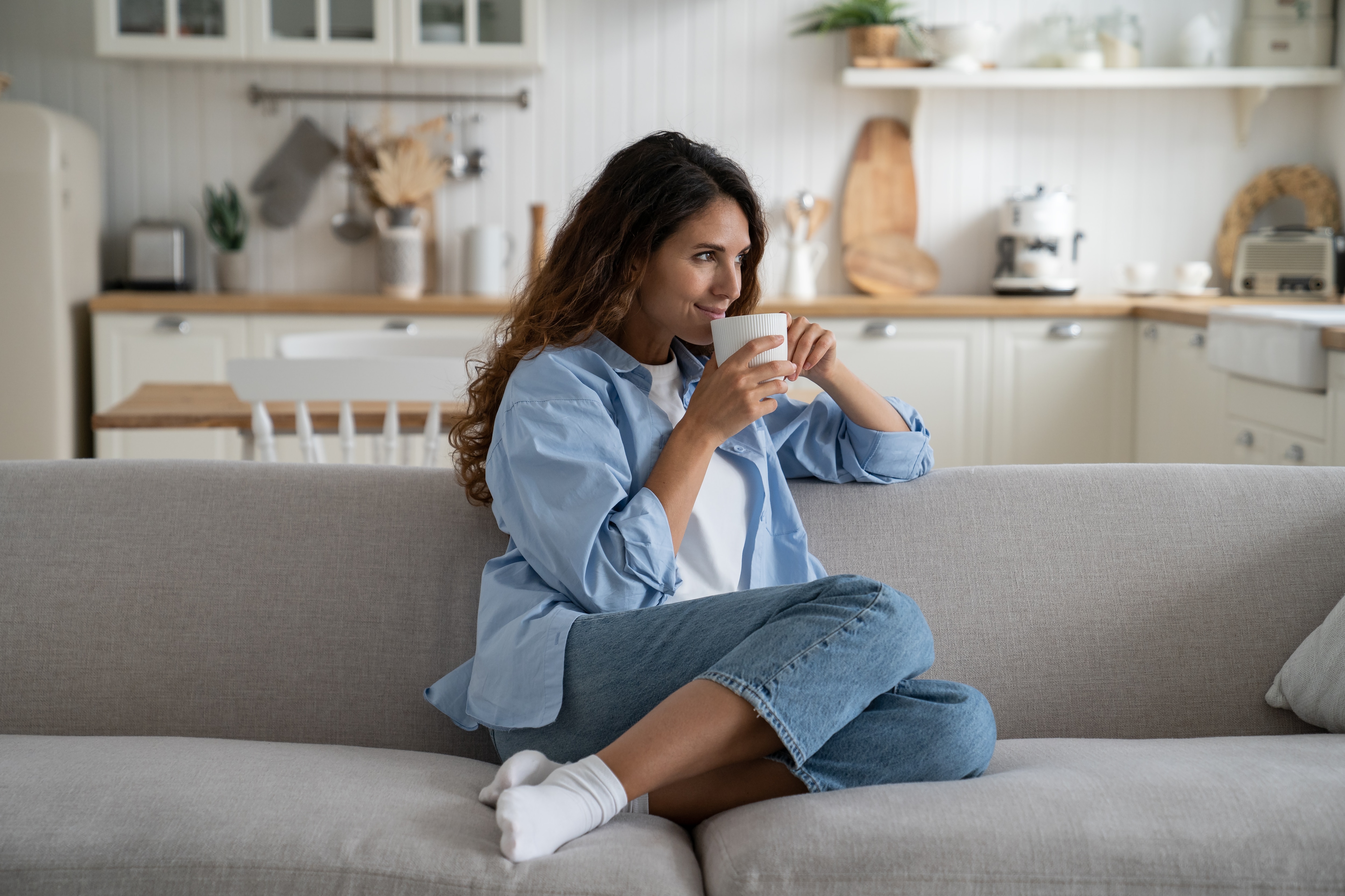 A woman contently relaxing on her couch with a warm cup of herbal tea.