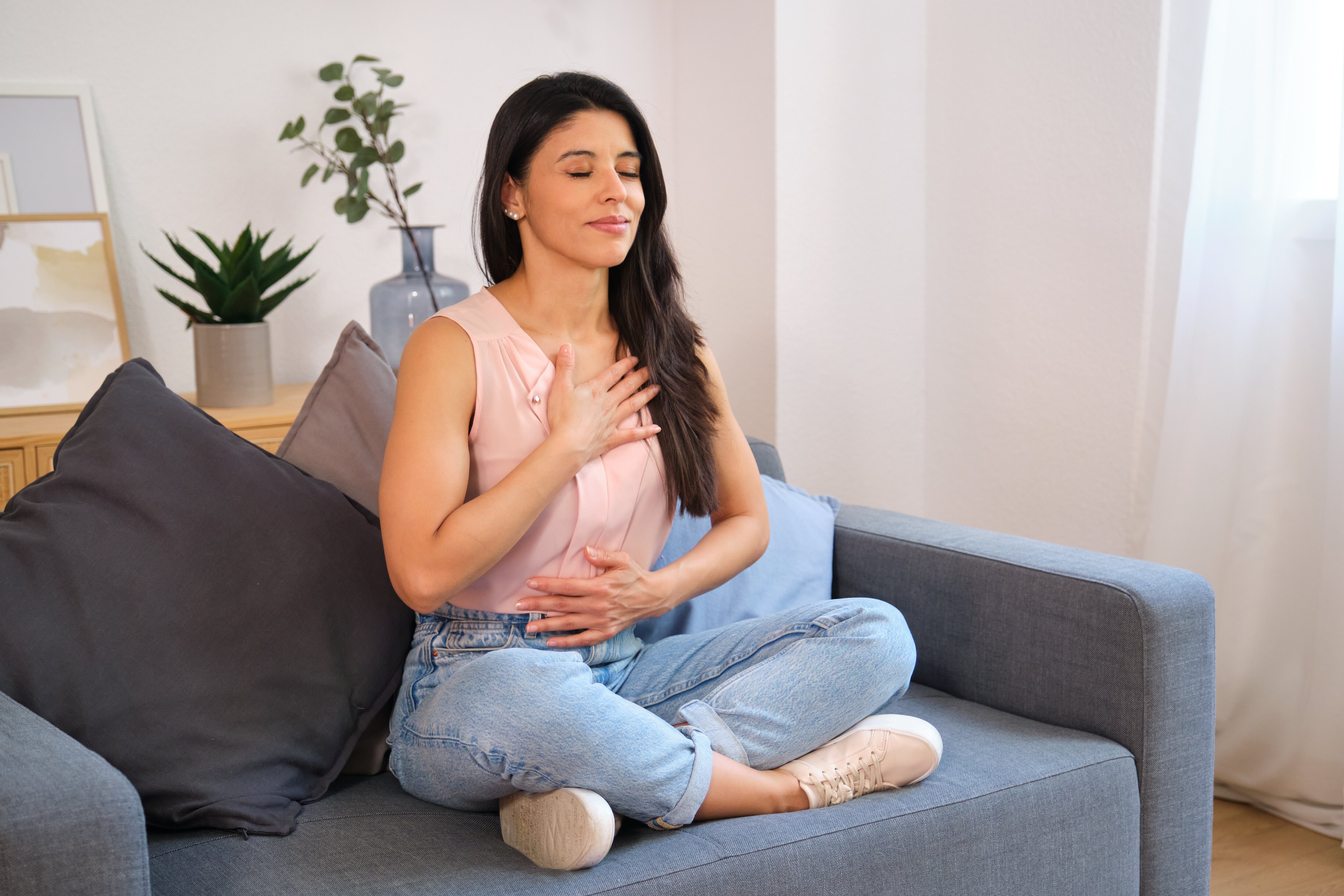 Mulher serena praticando exercícios de respiração profunda em casa no sofá